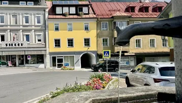 Historische Gebäudeansicht mit gelber Fassade, Solarpaneelen auf dem Dach und einem Brunnen im Vordergrund.