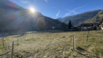 Sonniges Grundstück mit weitem Blick auf die umliegende Berglandschaft und grüne Wiesen.
