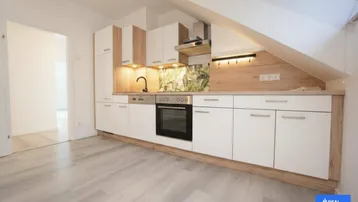 Moderne Einbauküche im Dachgeschoss mit weißen Fronten, Holzakzenten und integrierten Geräten.