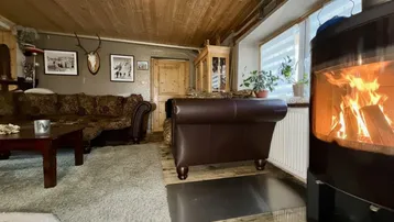 Rustikales Wohnzimmer mit Holzbalkendecke, Kaminofen und gemütlicher Sitzecke.