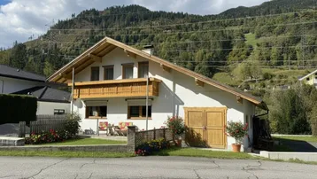 Traditionelles Haus mit Balkon und Gartenbereich vor alpiner Bergkulisse.