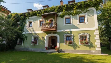 Traditionelles Haus mit grüner Fassade, bewachsenem Dach, kleinem Holzbalkon und gepflegtem Vorgarten.
