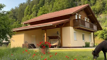 Ländliches Haus mit rotem Ziegeldach, Holzbalkonen und einem blühenden Garten in den Bergen.