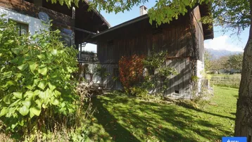 Blick auf das rustikale Holzhaus mit gepflegtem Garten und herbstlicher Bepflanzung unter blauem Himmel.