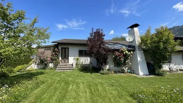 Einfamilienhaus mit großem Garten und gepflegter Rasenfläche unter blauem Himmel.