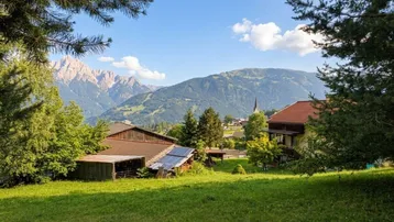 Panoramablick auf die umliegende Berglandschaft mit traditionellen Häusern und grünen Wiesen unter blauem Himmel.