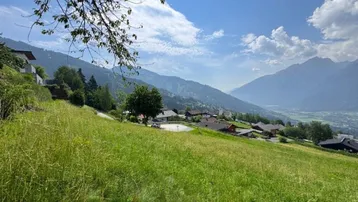 Weitläufige grüne Wiese mit Blick auf die umliegende Berglandschaft und Siedlung.