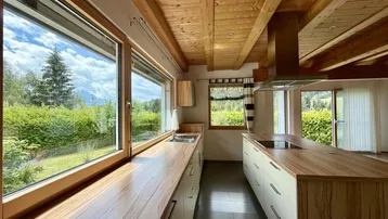 Helle Küche mit Holzbalkendecke, großen Fenstern und Blick ins Grüne.