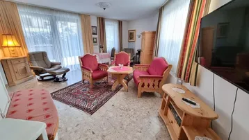 Gemütliches Wohnzimmer mit traditionellen Holzmöbeln, Teppichen und Zugang zum Balkon.