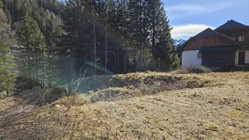Weitläufiges Grundstück in alpiner Umgebung mit altem Gebäude und Bergblick.