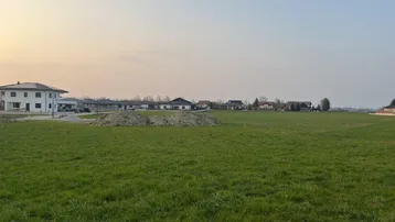 Weitläufiges grünes Feld mit Blick auf umliegende Wohnhäuser und Bauland unter klarem Himmel.