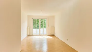 Geräumiger, heller Wohnraum mit Parkettboden und Zugang zu einem französischen Balkon.