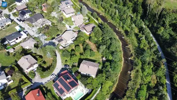 Luftaufnahme einer Wohnsiedlung mit Häusern, viel Grün, einem Fluss und Stromleitungen.