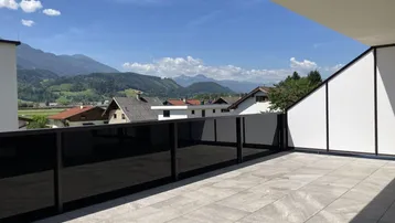 Sonniger Balkon mit weitem Ausblick über die Dächer und die majestätischen Berge im Hintergrund.