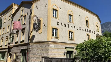 Traditionelles Gasthausgebäude mit gelben Akzenten und grünen Türen unter blauem Himmel.