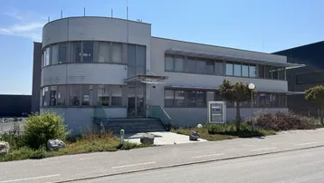 Modernes Bürogebäude mit abgerundeter Fassade und großen Fenstern an einer Straße gelegen.