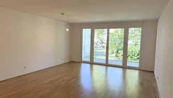 Helles Wohnzimmer mit Parkettboden und großen Fenstern, die Zugang zu einem Balkon bieten.