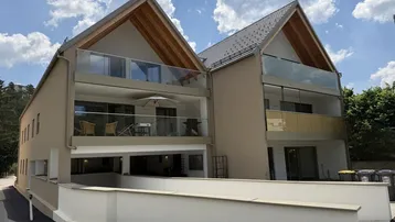Modernes Mehrfamilienhaus mit mehreren Balkonen, Satteldach und heller Fassade, umgeben von Grün.