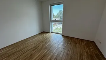 Helles Schlafzimmer mit Parkettboden und großem Fenster mit Blick ins Grüne.