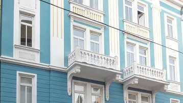 Historische Fassade eines Altbaus in Blau und Weiß mit dekorativen Balkonen und großen Fenstern.