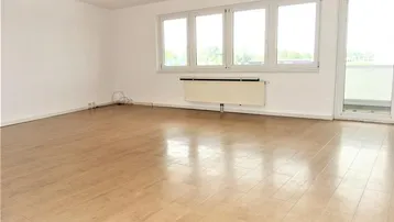 Helles, unmöbliertes Wohnzimmer mit Parkettboden, großen Fenstern und Zugang zum Balkon.