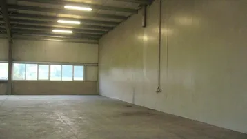 Geräumige, leere Lagerhalle mit hohen Decken, Betonboden und Oberlichtern, die viel natürliches Licht hereinlassen.
