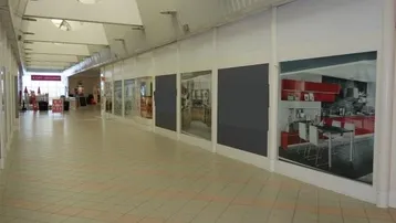 Heller, langer Flur in einem Gewerbegebäude mit großen Schaufenstern und Tageslicht von oben.