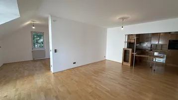 Geräumiger Wohnbereich mit hellem Parkettboden, weißen Wänden und integrierter Küche im Dachgeschoss.