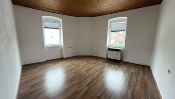 Geräumiger Raum mit Holzbalkendecke und Laminatboden, ideal als Wohn- oder Schlafzimmer nutzbar.
