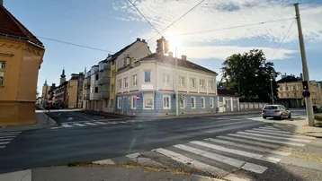 Das Eckgebäude präsentiert sich an einer belebten Kreuzung mit blauer und beiger Fassade unter strahlendem Himmel.