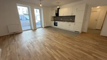 Heller Wohn-Essbereich mit Parkettboden, integrierter Küche und Zugang zur Terrasse.