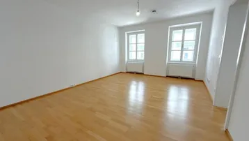 Helles, leeres Wohnzimmer mit Parkettboden und zwei Fenstern, bereit zur individuellen Gestaltung.