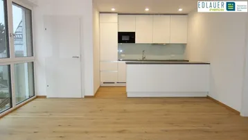 Moderner Wohn-Essbereich mit integrierter Küche, hellen Oberflächen und Holzboden.