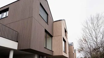 Moderne Reihenhäuser mit Holzfassade und großen Fenstern unter bewölktem Himmel.