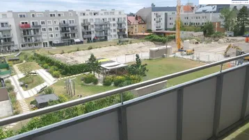 Blick vom Balkon auf eine Grünfläche, weitere Gebäude und eine Baustelle in der Ferne.