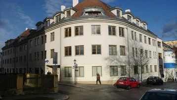 Gebäude mit markanter runder Fassade, vielen Fenstern und kleinen Balkonen unter einem blauen Himmel.
