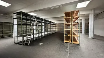 Geräumiger Lagerraum mit hohen Regalen und Betonboden, bereit für die Nutzung und mit Gebrauchsspuren.