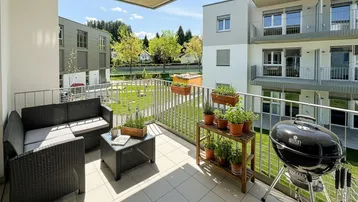 Geräumiger Balkon mit Sitzgelegenheiten, Grill und Blick auf die umliegenden Gebäude und Grünflächen.