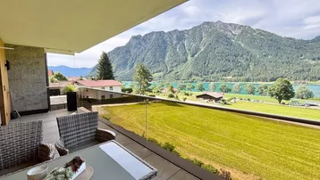 Möblierter Balkon mit Glasgeländer und atemberaubendem Blick auf den See und die Berge.