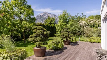 Geräumige Holzterrasse mit üppiger Bepflanzung und beeindruckendem Bergblick unter blauem Himmel.