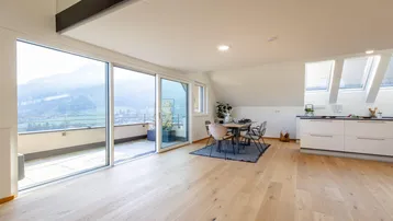 Heller Wohnbereich mit offener Küche, Essbereich und Zugang zu einer großen Terrasse mit Bergblick.