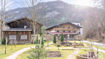 Traditionelle Gebäude in alpiner Landschaft mit Bergen im Hintergrund und sonnigem Wetter.