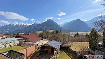 Gartenbereich mit Holzterrasse, Rasenfläche, Gartenhaus und beeindruckendem Bergblick.