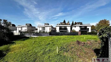 Blick auf ein grünes Grundstück mit modernen Neubauten im Hintergrund unter blauem Himmel.