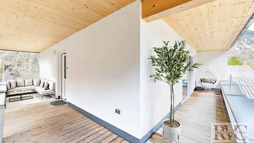 Geräumiger, überdachter Balkon mit Holzboden, Sitzgelegenheiten und Blick ins Grüne.