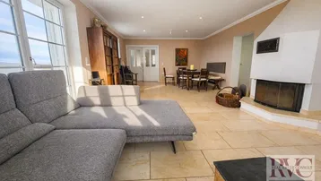 Helles Wohn- und Esszimmer mit Kamin, großem Sofa und Zugang zu einem Balkon.
