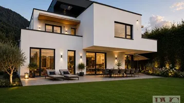 Moderne weiße Villa mit Flachdach, großen Fenstern, möblierter Terrasse und gepflegtem Rasenbereich am Abend.