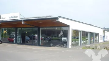 Außenansicht eines modernen Autohauses mit großer Glasfassade und Kundenparkplätzen unter einem klaren Himmel.