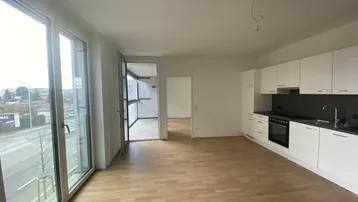 Heller Wohn- und Kochbereich mit moderner Einbauküche, Parkettboden und Zugang zur Loggia.