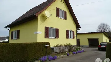 Gelbes Einfamilienhaus mit braunen Fensterläden, Vorgarten und separater Garage.